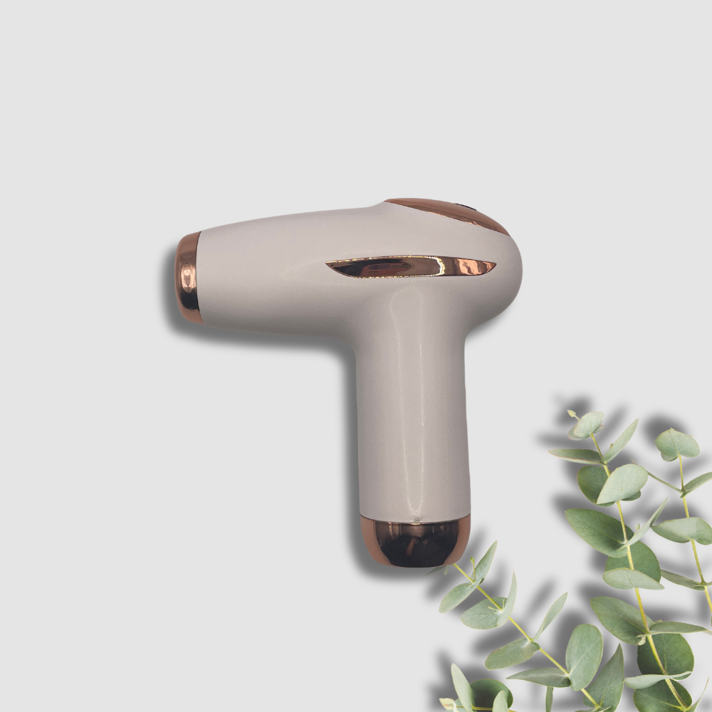 Beige fascia compact massage gun with gold with rose gold accents on a light gray background with eucalyptus leaves