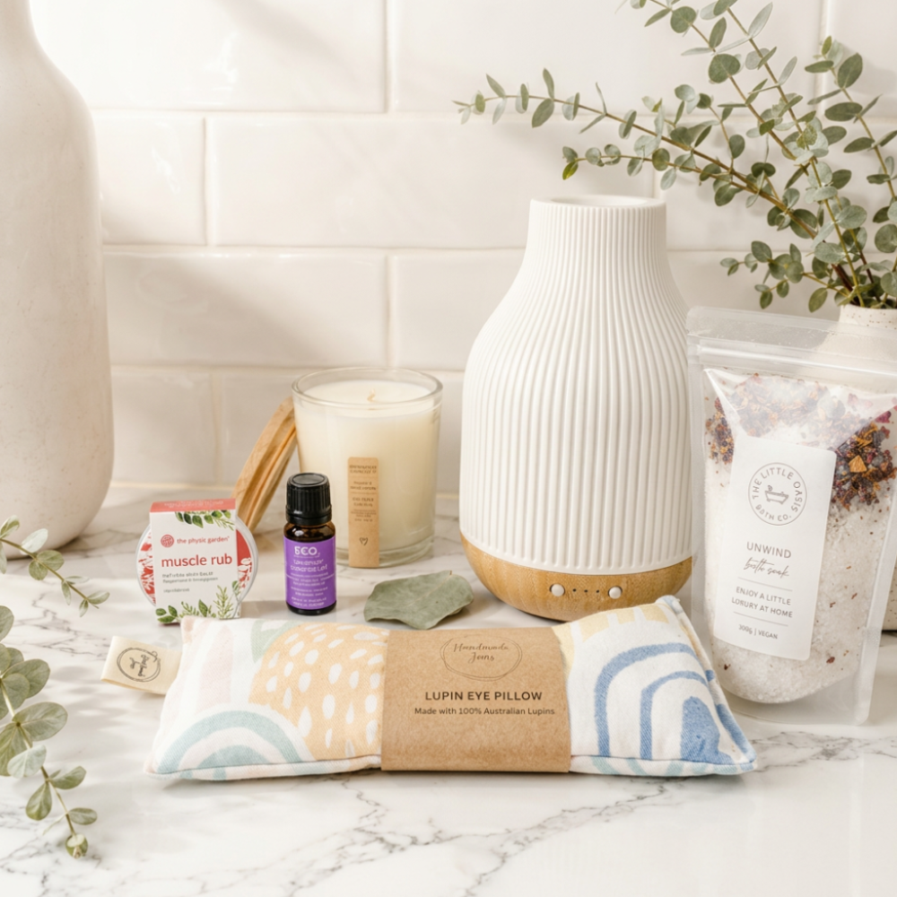 Lifestyle image of a marble surface with a coastal aromatherapy diffuser, lupin eye pillow, essential oil bottle, candle, and other wellness items.