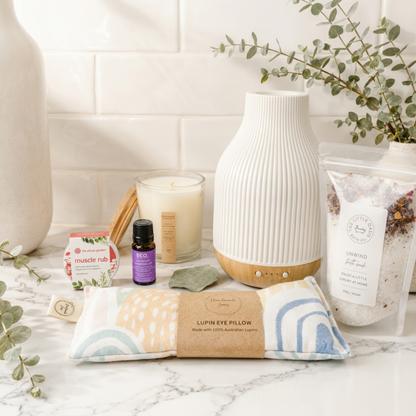 Lifestyle image of a marble surface with a coastal aromatherapy diffuser, lupin eye pillow, essential oil bottle, candle, and other wellness items.