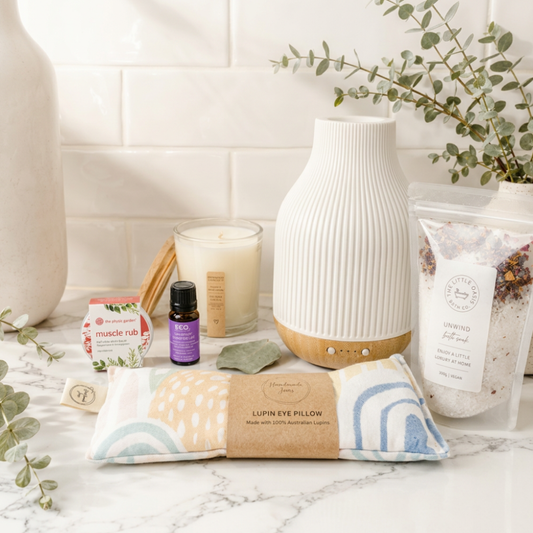 Lifestyle image of a marble surface with a coastal aromatherapy diffuser, lupin eye pillow, essential oil bottle, candle, and other wellness items.