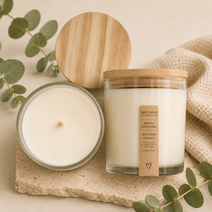 Two candles with wooden lids on a stone surface with eucalyptus leaves.